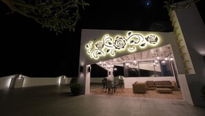 Un edificio moderno con un diseño iluminado único en la noche, que cuenta con un comedor con mesas y sillas, y una zona de estar con sofás.