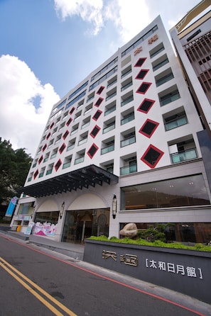 Un hotel moderno con una entrada destacada, varios pisos y una fachada distintiva con detalles rojos.
