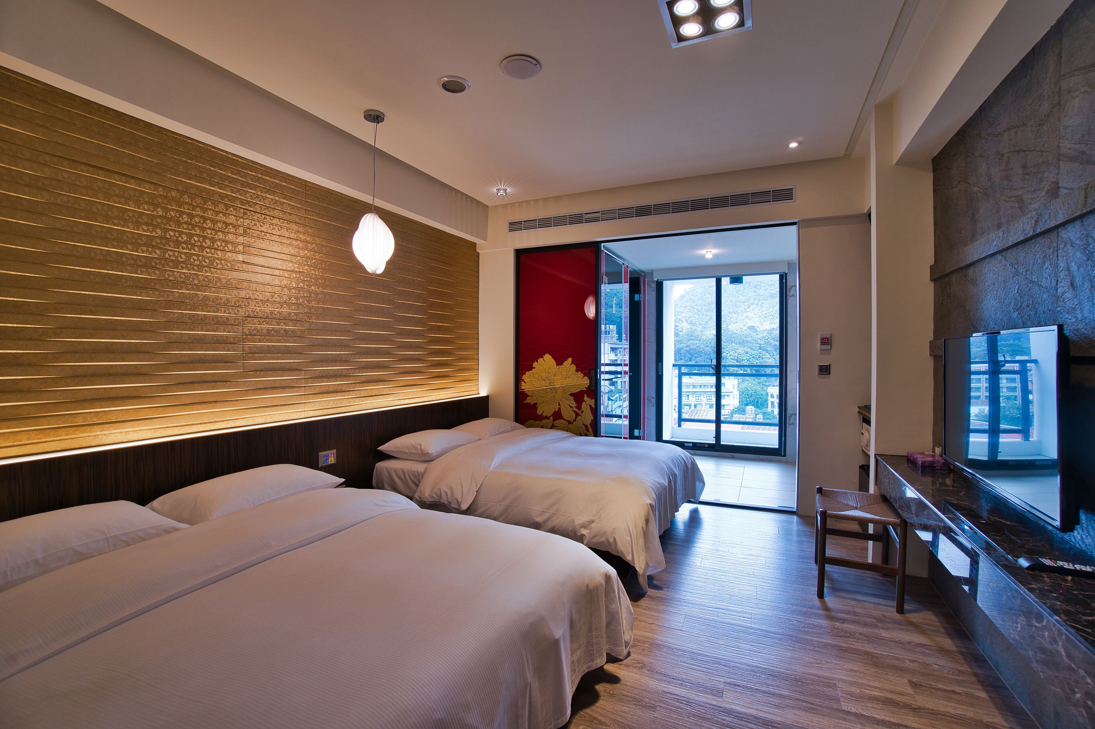 A hotel room with two beds, a bench, a TV, and a large window offering a city view.