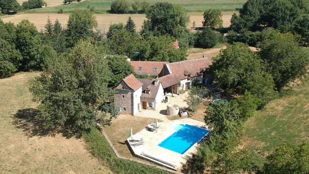 Vista aérea de una propiedad rural con una casa de piedra, una piscina y vegetación circundante.