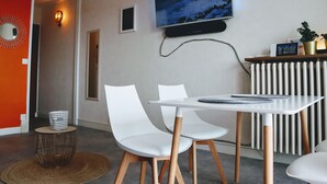 A modern living room with a white table and chairs, a mounted TV, and a red accent wall. - Pixie by the sea Design and connected apartment (La Baule-Escoublac)