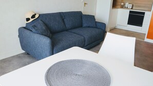 A modern living room with a blue sofa, a white table, and a kitchen area in the background. - Pixie by the sea Design and connected apartment (La Baule-Escoublac)