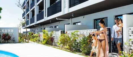 Un edificio moderno con piscina, rodeado de vegetación y una valla blanca.