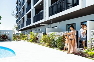 Un edificio moderno con piscina, rodeado de vegetación y una valla blanca.