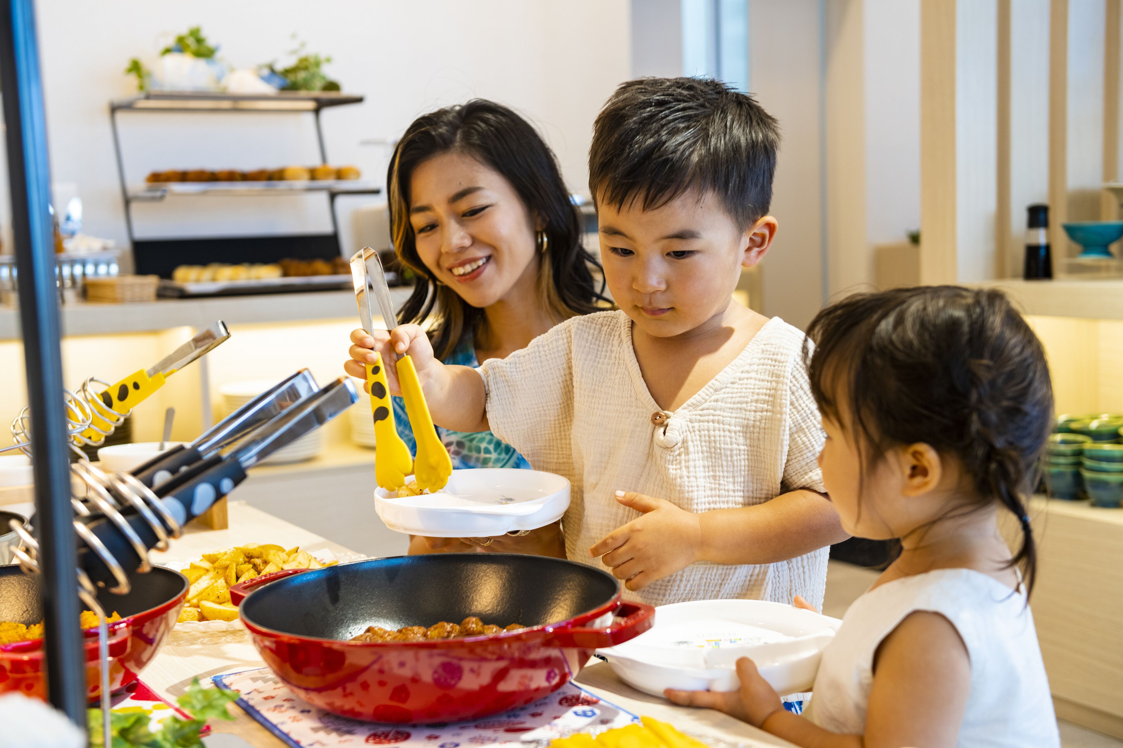 A family cooking together in a kitchen with a red pot, a white plate, and a shelf with baked goods in the background.