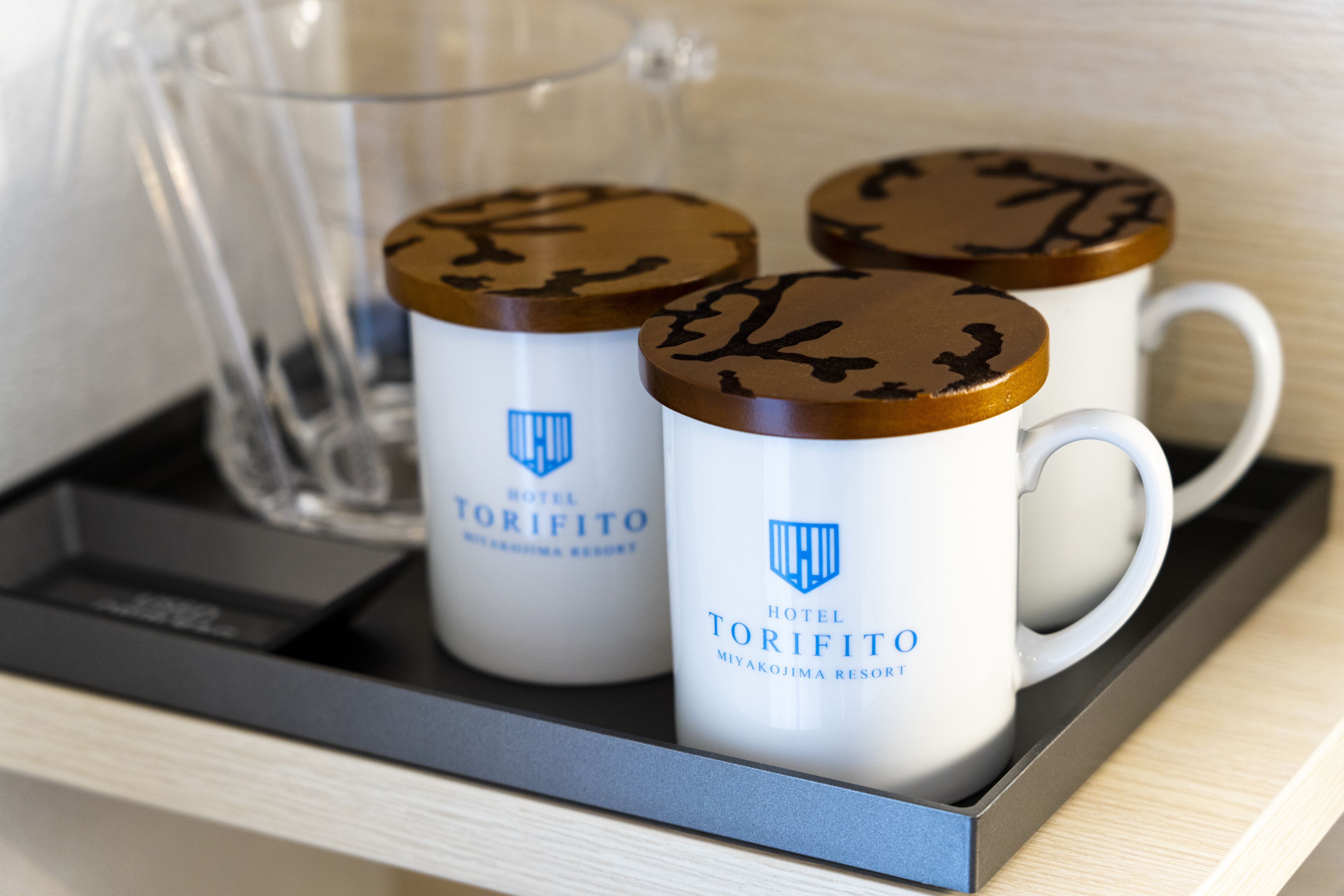 Three white mugs with brown lids and the Hotel Torifito logo, placed on a tray.