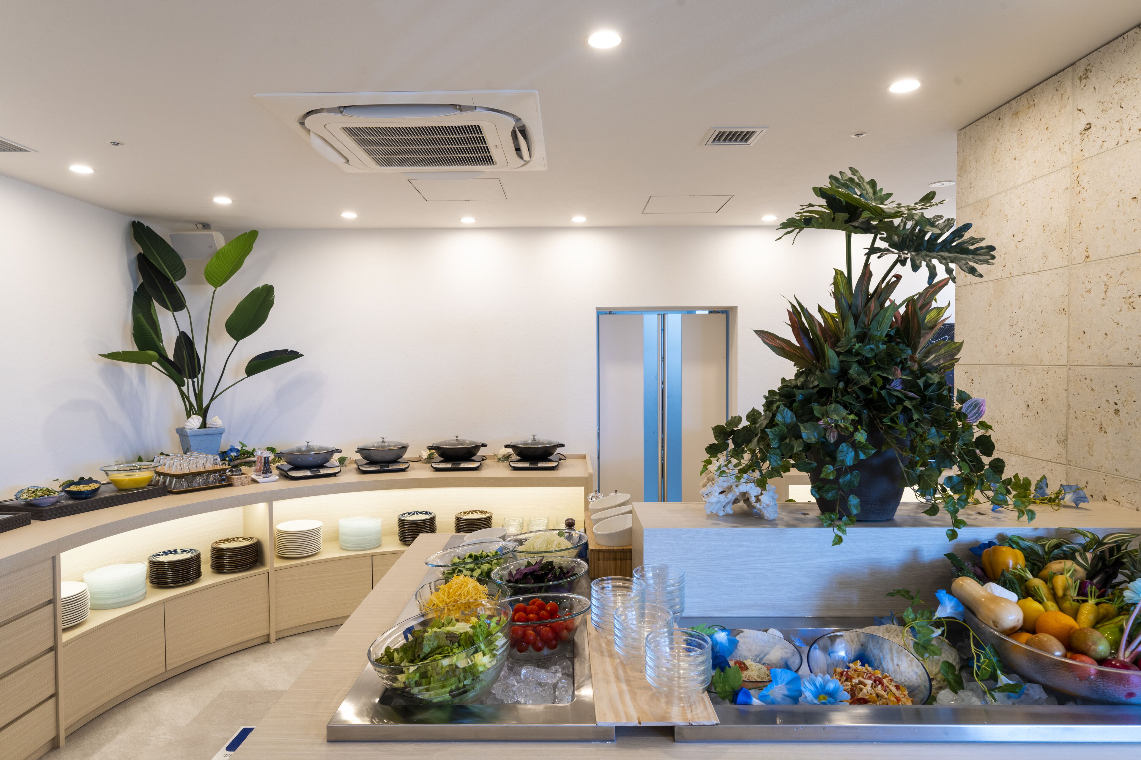 A buffet setup with various food items and a large potted plant.