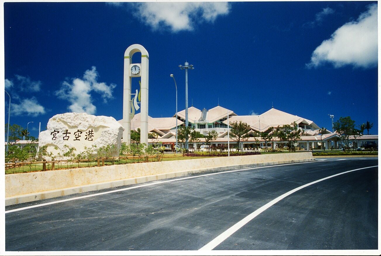 A modern building with a clock tower, a large rock, and a clear blue sky.