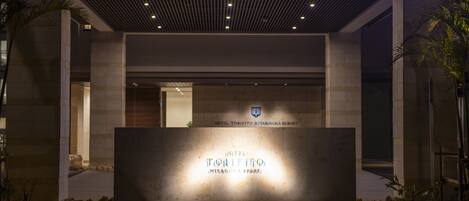 The exterior of Hotel Toritto Miyakojima Resort with a modern entrance and illuminated signage.