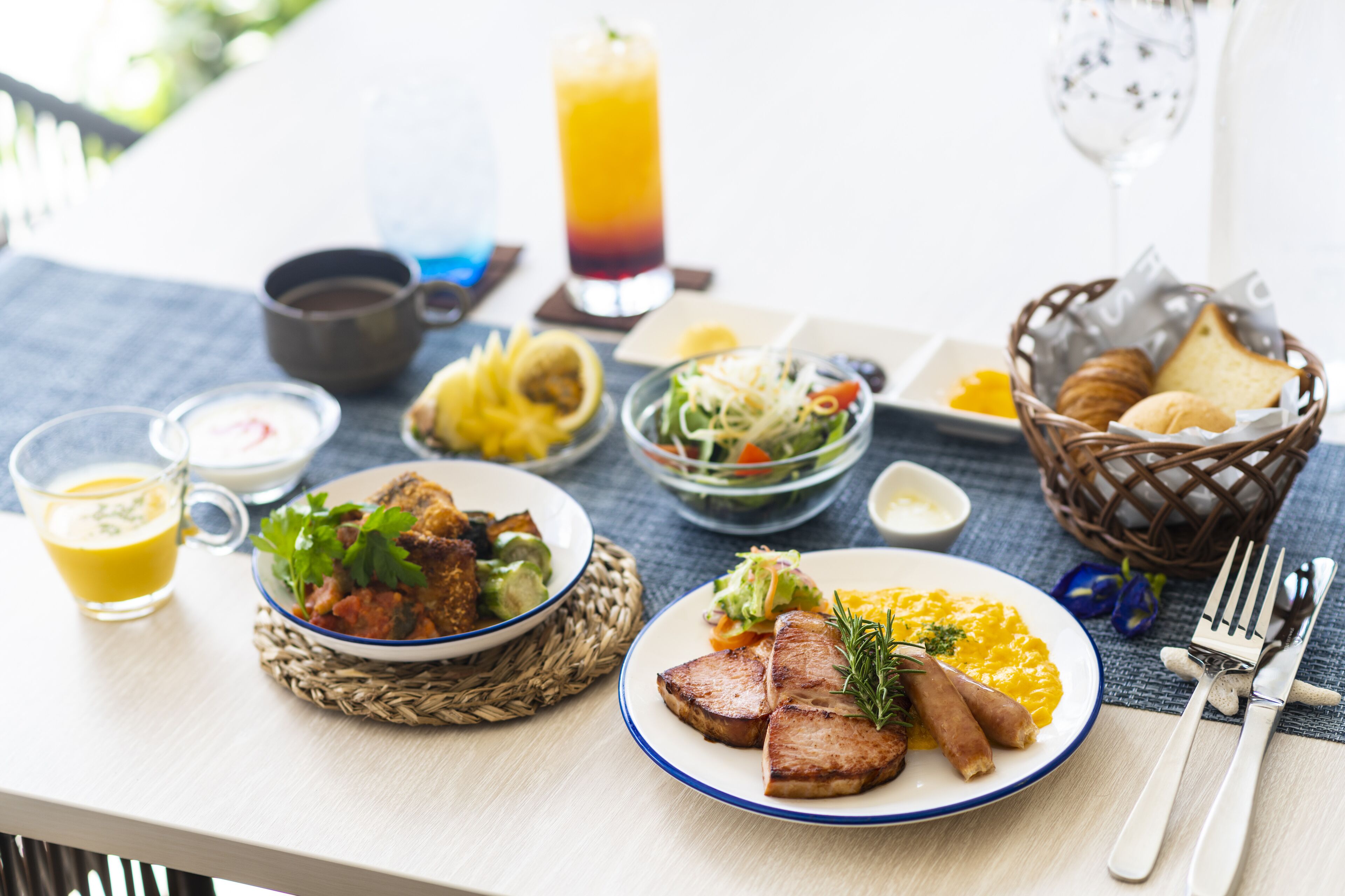 Ein Tisch mit Frühstücksangeboten, darunter Eier, Würstchen und ein Salat, zusammen mit einem Glas Orangensaft und einem Glas rotem Saft.