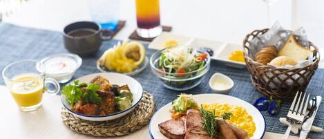 Ein Tisch mit Frühstücksangeboten, darunter Eier, Würstchen und ein Salat, zusammen mit einem Glas Orangensaft und einem Glas rotem Saft.