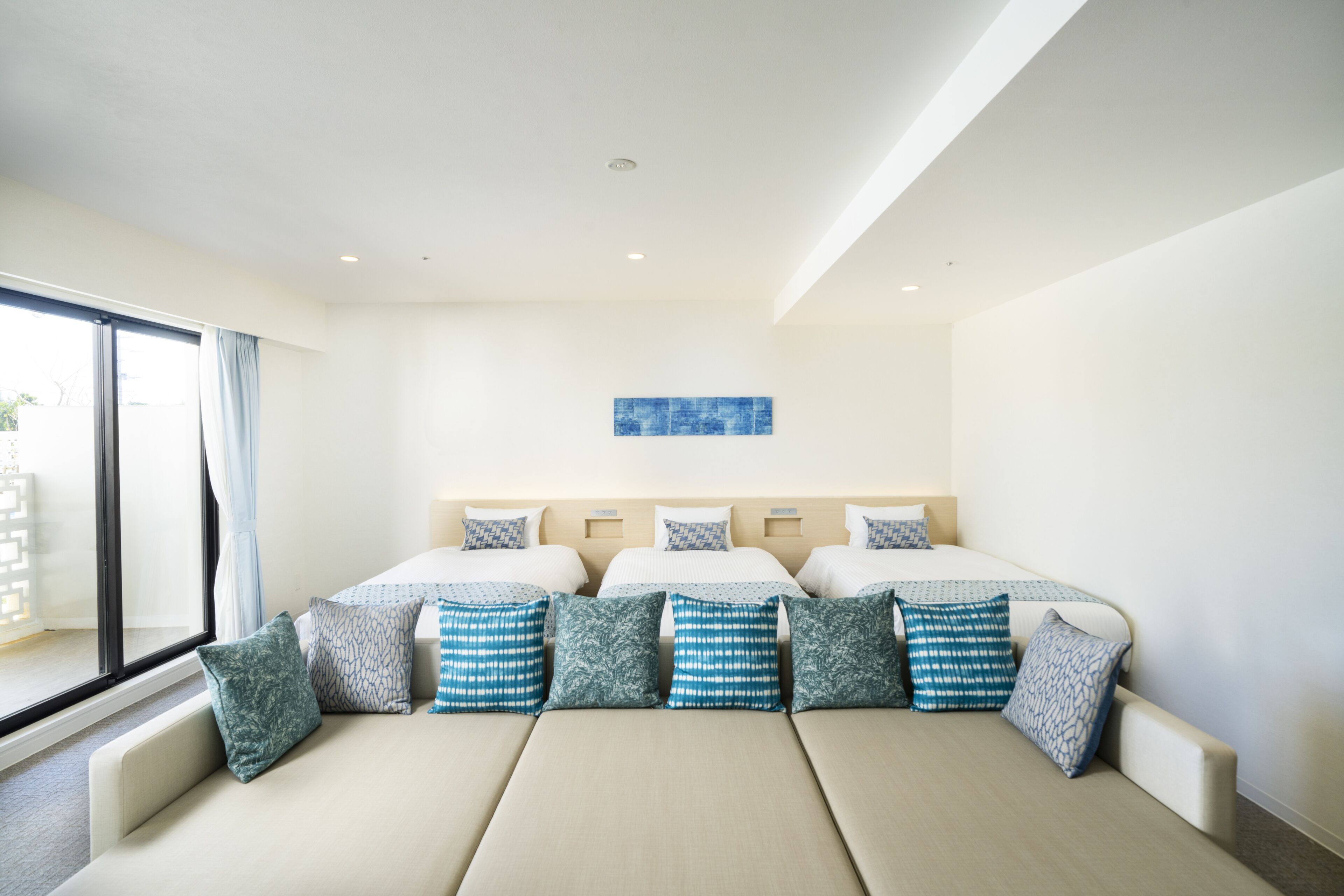 Una habitación de hotel con una cama grande, un sofá, una ventana con cortinas y una obra de arte azul en la pared.