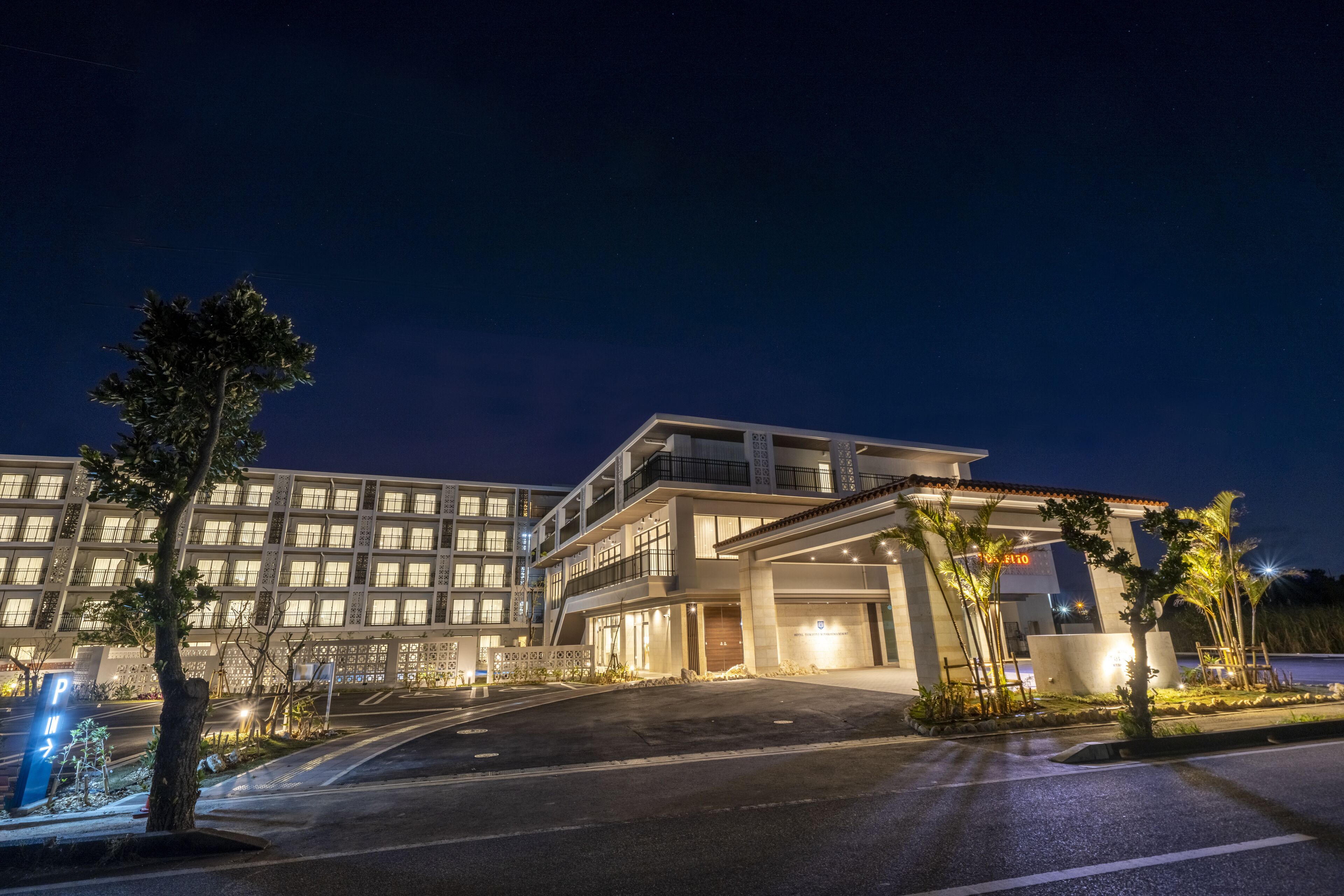 Ein modernes Hotel mit mehrstöckiger Bauweise, beleuchtetem Eingangsbereich und gepflegter Umgebung.
