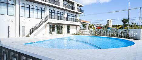 A modern building with a large swimming pool, multiple balconies, and a staircase leading to the upper floors.