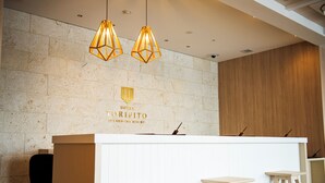 Un comptoir d’accueil avec un mur en pierre en arrière-plan, deux suspensions lumineuses et un panneau en bois sur le côté droit.