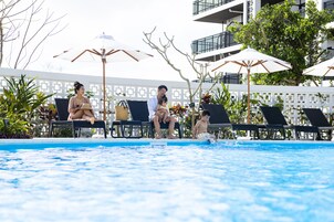 Una piscina al aire libre, sombrillas, sillones reclinables de piscina