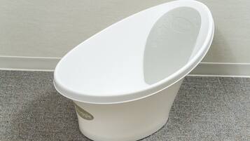 A white trash bin with a lid, placed on a carpeted floor against a wall.
