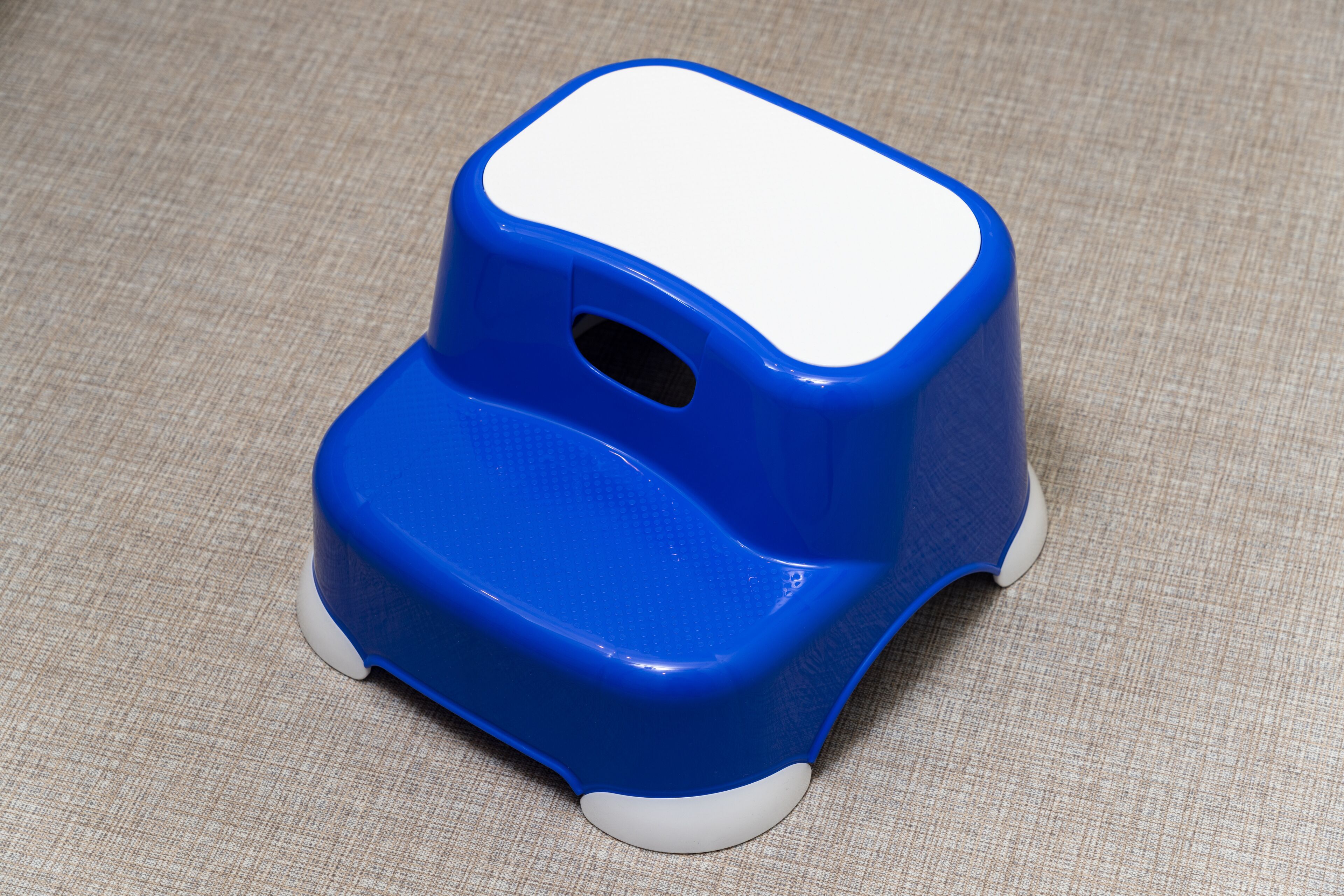 A blue and white plastic stool with a hole in the backrest, placed on a textured fabric surface.