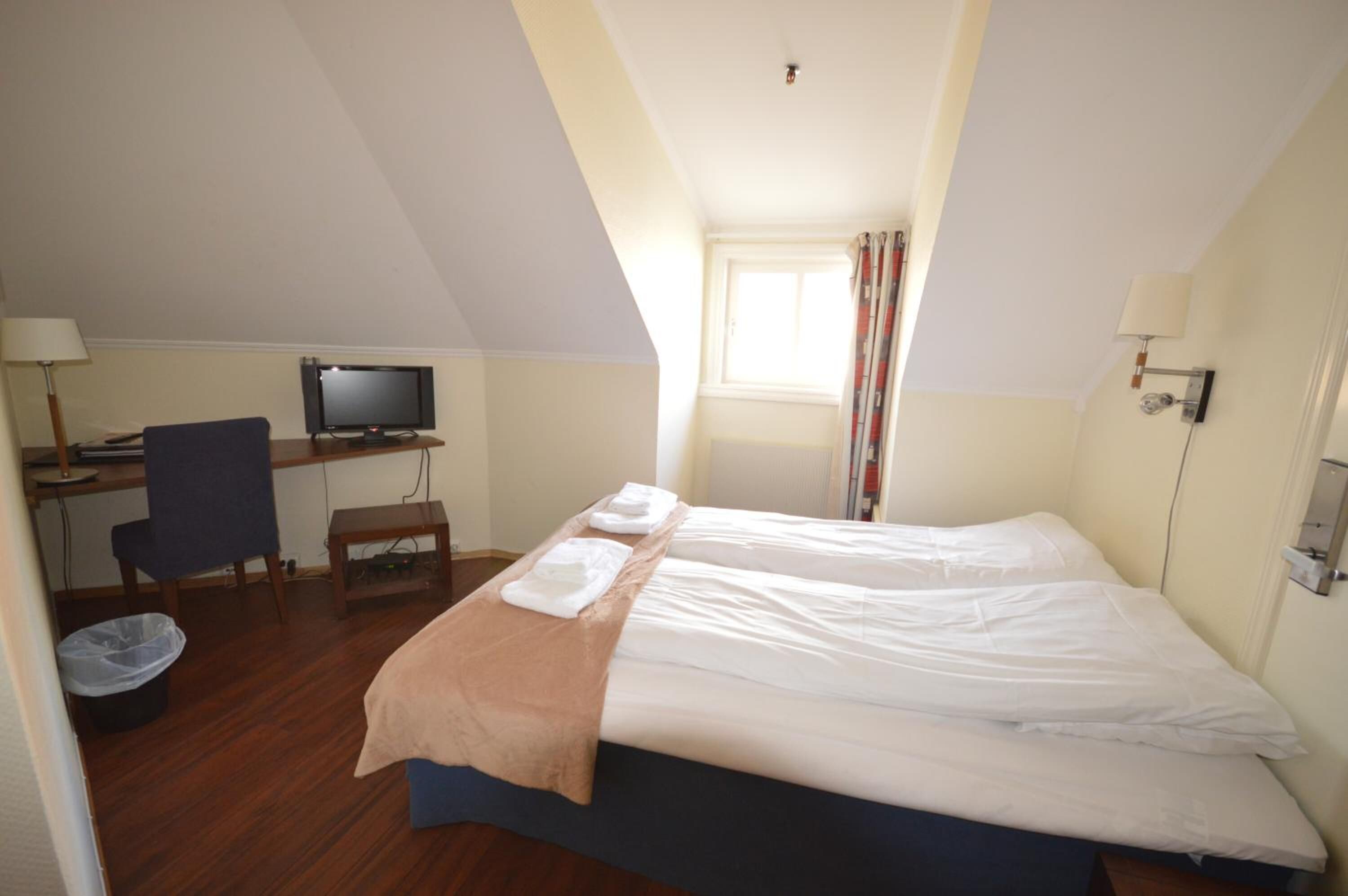 A hotel room with a bed, a desk with a computer, a chair, and a window.