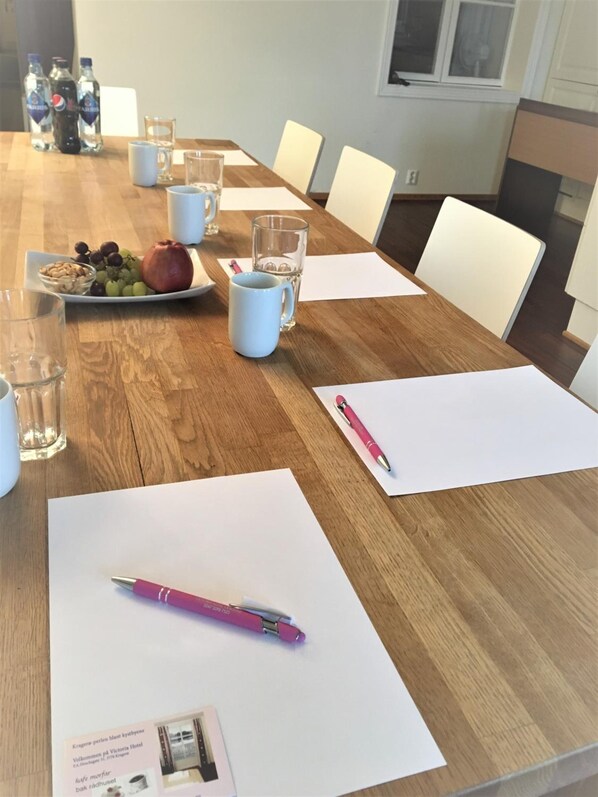 A wooden conference table with water bottles, a plate of fruit, and a pink pen on a white paper. - Victoria Hotel (Kragero)