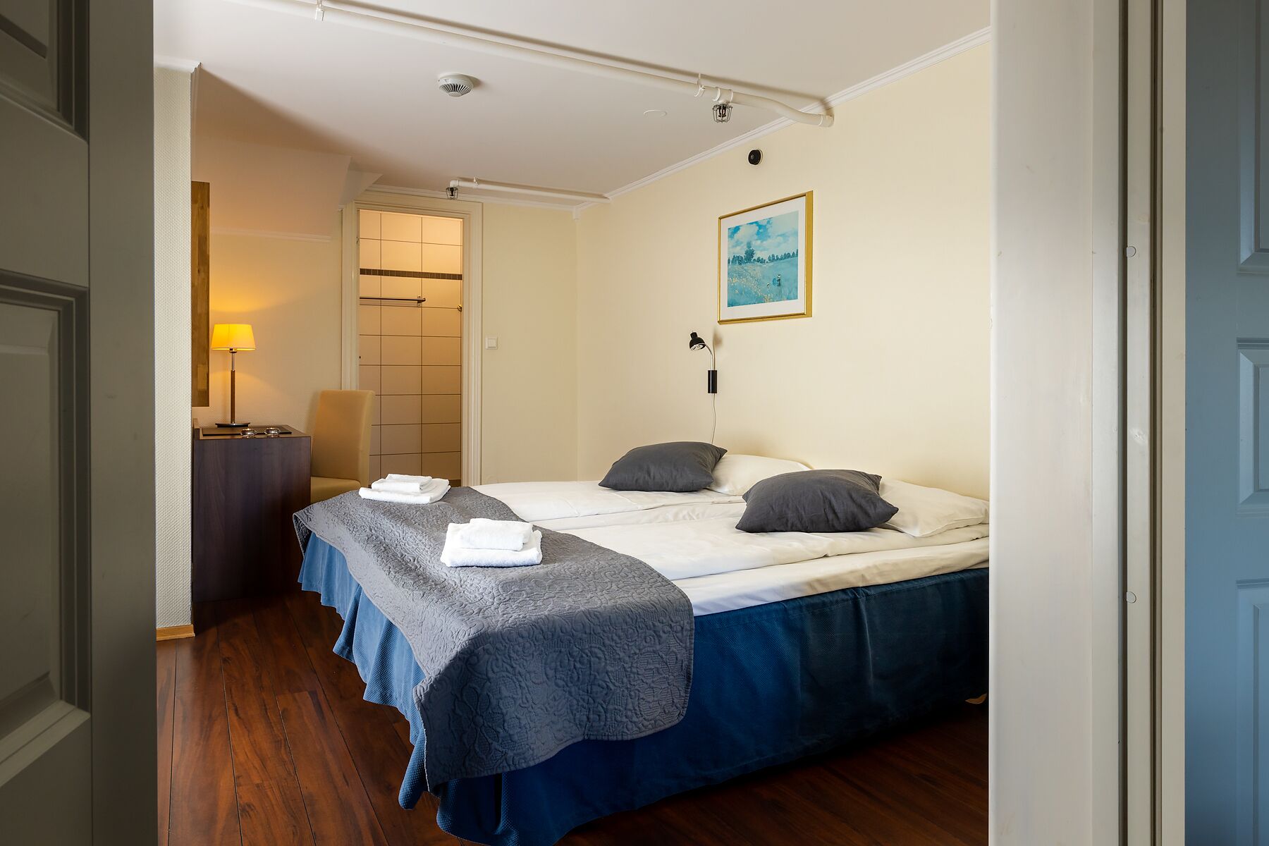 Ein Hotelzimmer mit einem Bett, einem Schreibtisch, einem Stuhl, einer Lampe und einem Bild an der Wand.