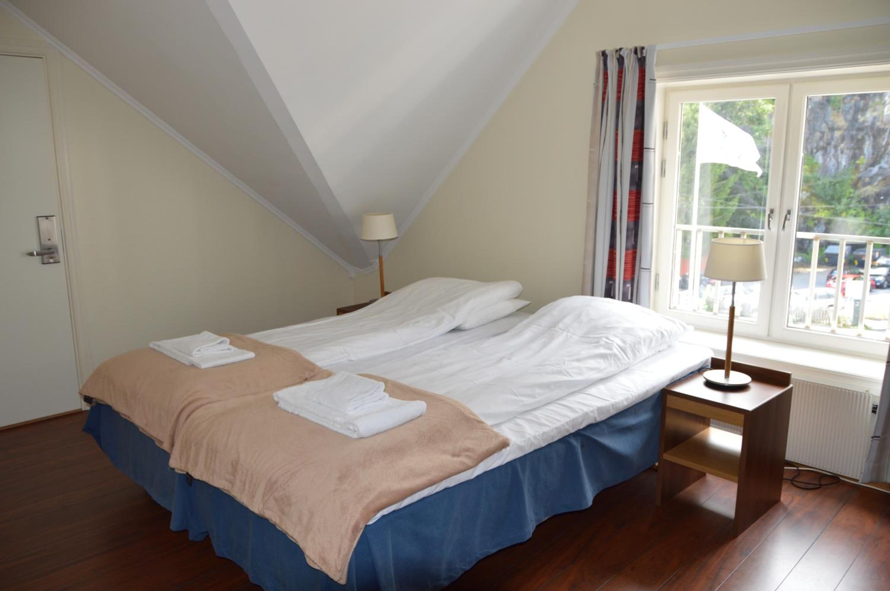 A bedroom with two beds, a window with curtains, a lamp, and a radiator.