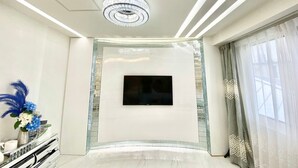 A modern living room with a flat-screen TV mounted on the wall, a decorative chandelier, and a sleek, reflective floor. - Reimi Mondo (Tokyo)