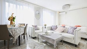 A modern living room with a white sofa, a glass coffee table, and a dining area with a table set for two. - Reimi Mondo (Tokyo)