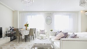 A modern hotel room with a white color scheme, a dining area with a table and chairs, a sofa, and a large mirror on the wall. - Reimi Mondo (Tokyo)