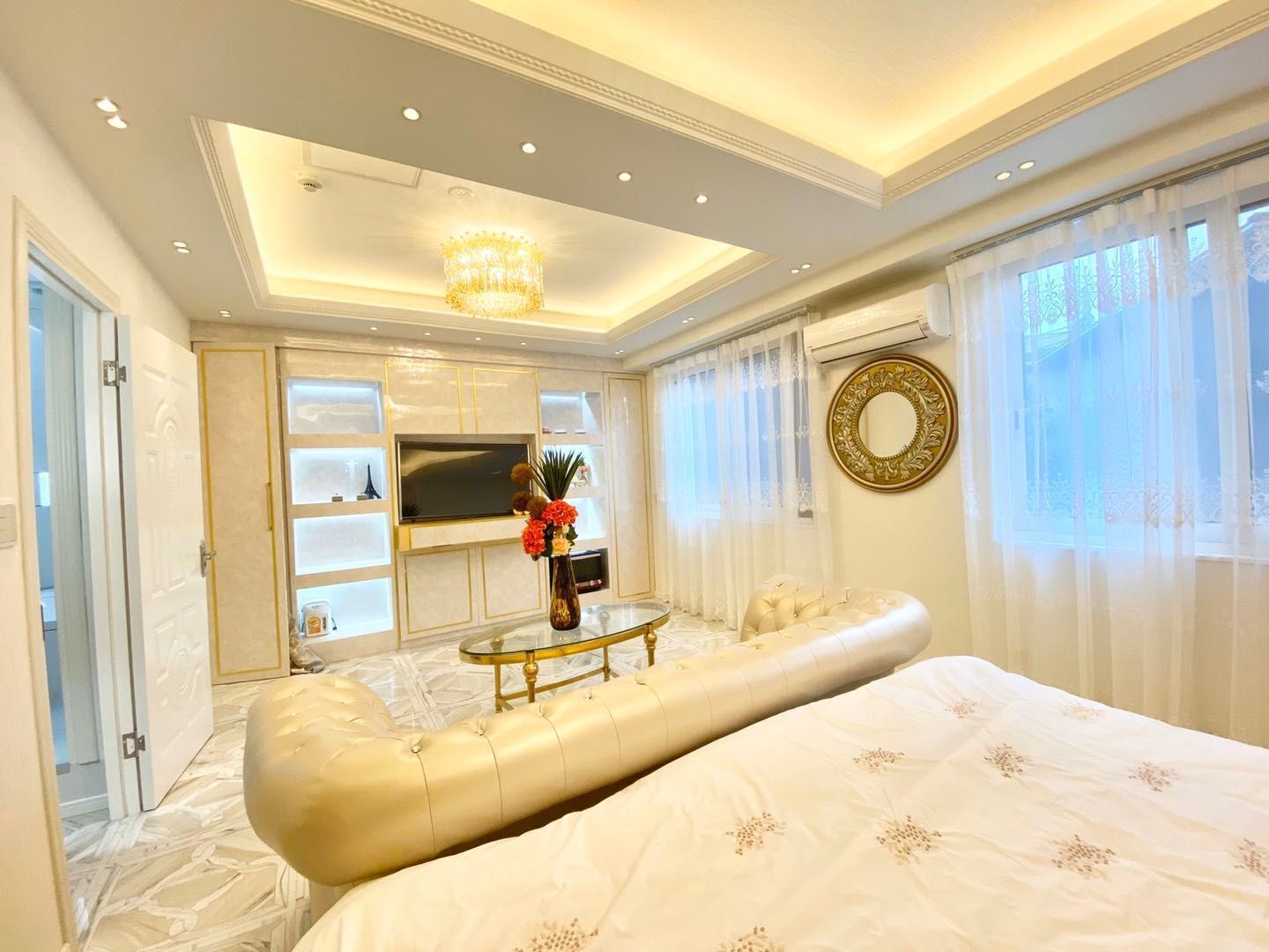 A luxurious bedroom with a large bed, a television, a glass coffee table, and a chandelier.