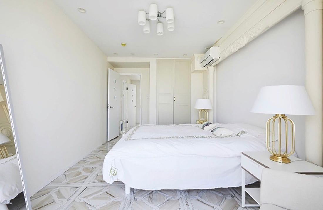 A hotel room with a large bed, two bedside tables with lamps, a mirror, and a door leading to another room.