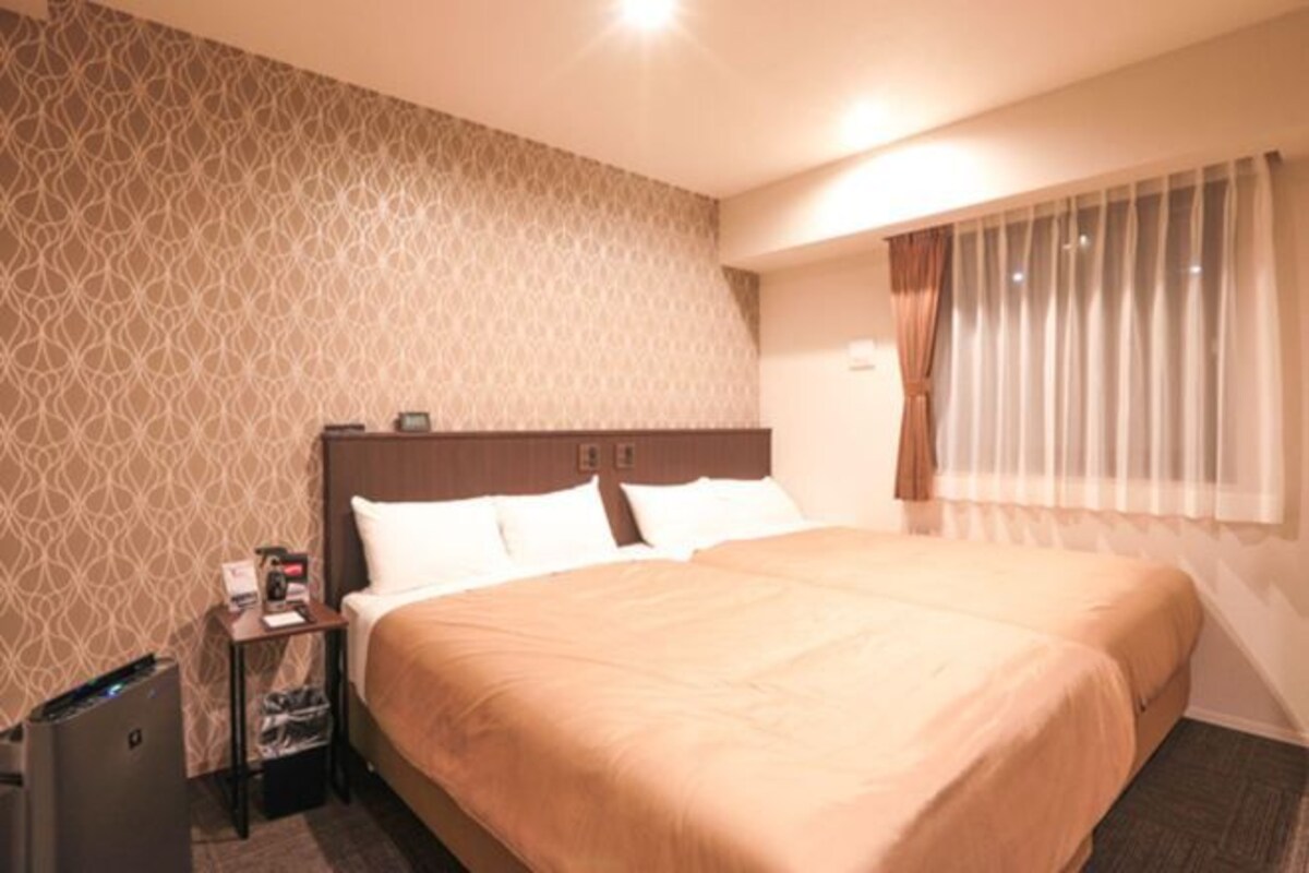 A hotel room with a large bed, a nightstand, and a window with curtains.