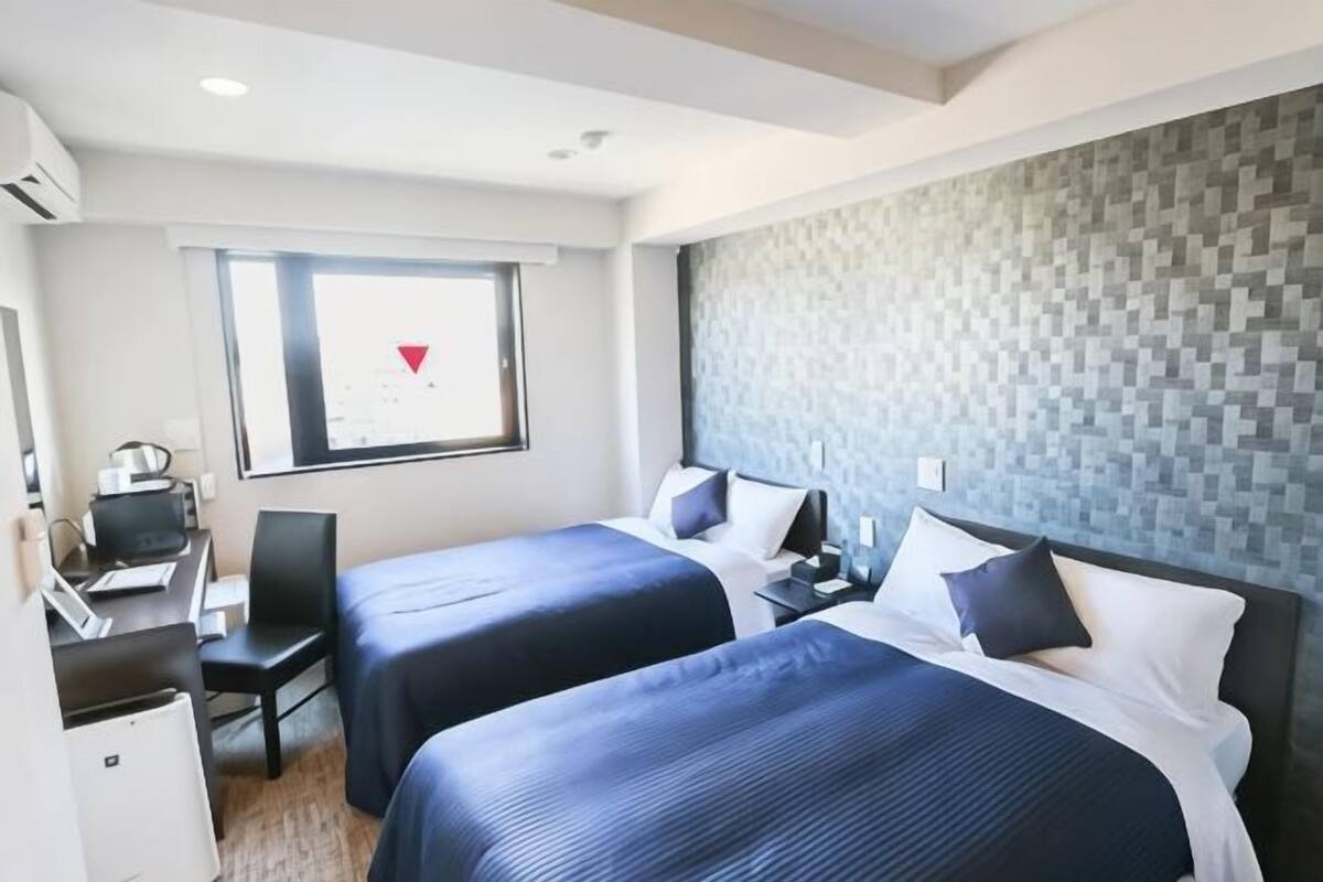 Hotellihuone, jossa on kaksi sänkyä, työpöytä, tuoli ja ikkuna.