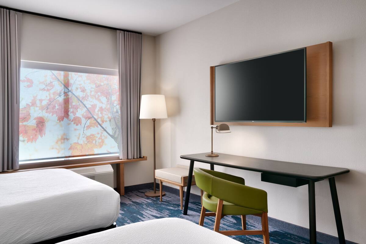Habitación de hotel con dos camas, un escritorio, una silla, un televisor y una ventana con cortinas.