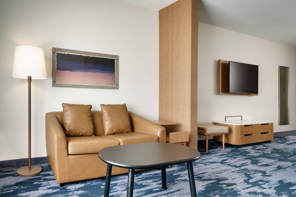 Habitación de hotel con sofá, una mesita, lámpara de pie, televisor y un mueble de madera.