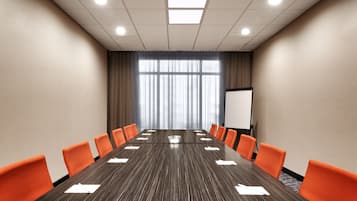 A conference room with a long table, orange chairs, a whiteboard, and a large window with curtains.