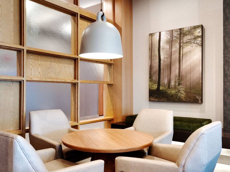 A modern interior with a round wooden table surrounded by four chairs, a large hanging light fixture, and a forest-themed painting on the wall.