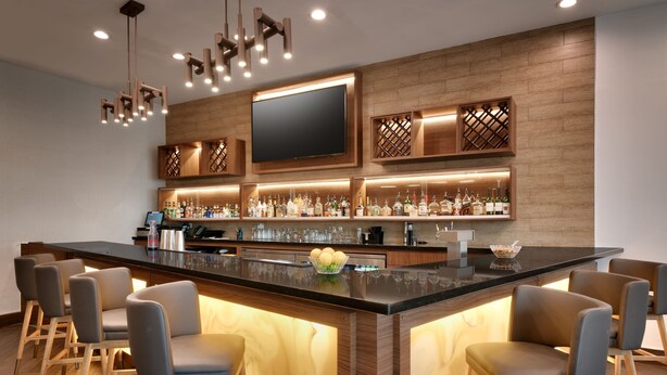 A modern bar area with a large island, bar stools, and a flat-screen TV mounted on the wall.