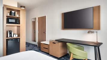 Ein Hotelzimmer mit einem Bett, einem Schreibtisch mit Stuhl, einer Mikrowelle, einer Kaffeemaschine und einem Fernseher.