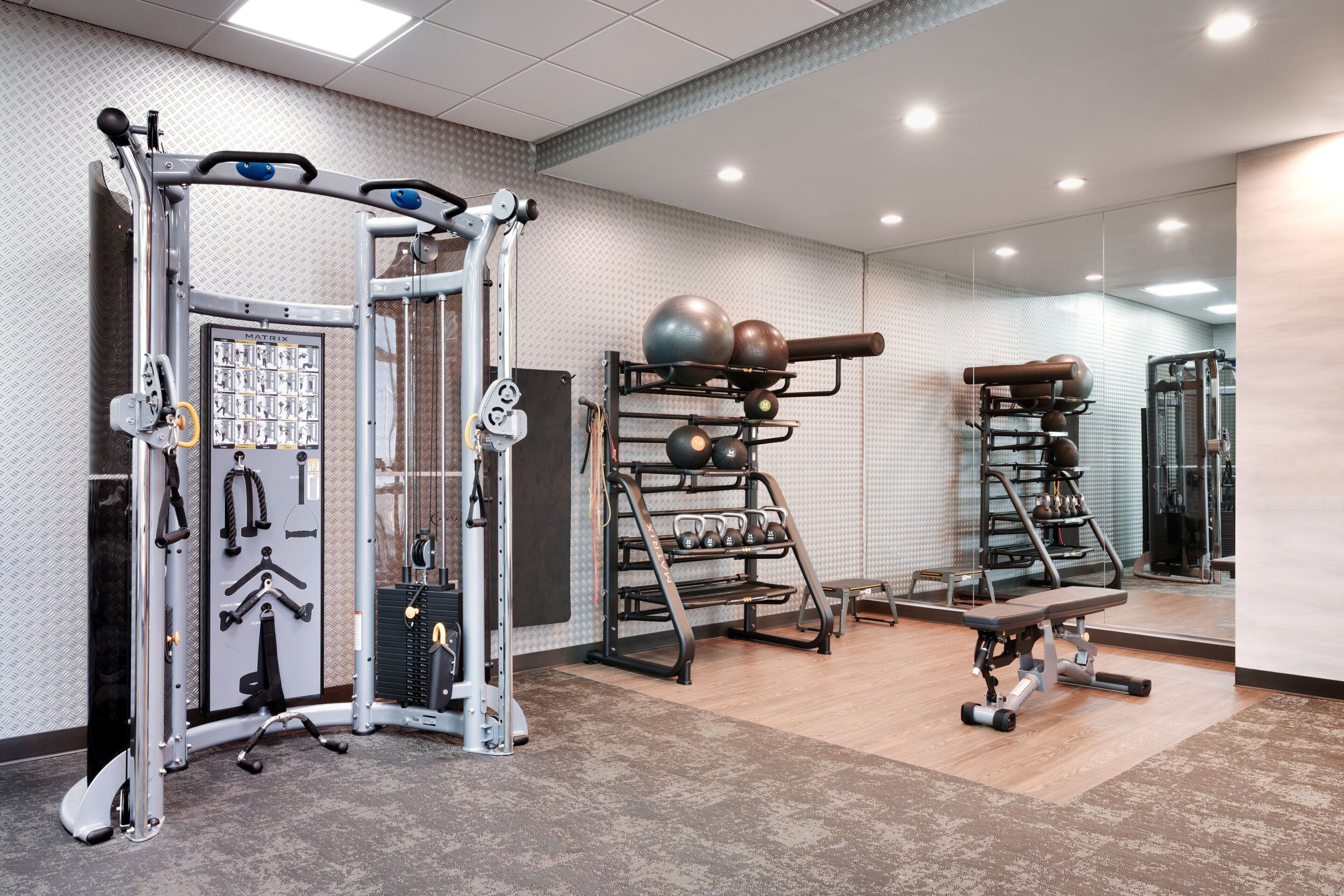 Un gimnasio con equipo de ejercicio diverso, un espejo grande y un suelo con diseño.