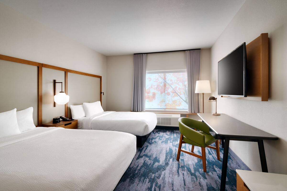 Habitación de hotel con dos camas, un escritorio, una silla, un televisor y una ventana con cortinas.