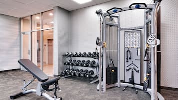 Uma academia com um banco, halteres e máquinas de musculação.
