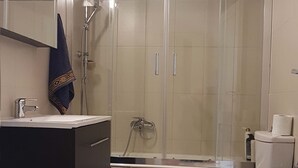 A bathroom with a shower, toilet, sink, and a towel hanging on the wall. - Olive Stonehouse Orestis (Kalamata)