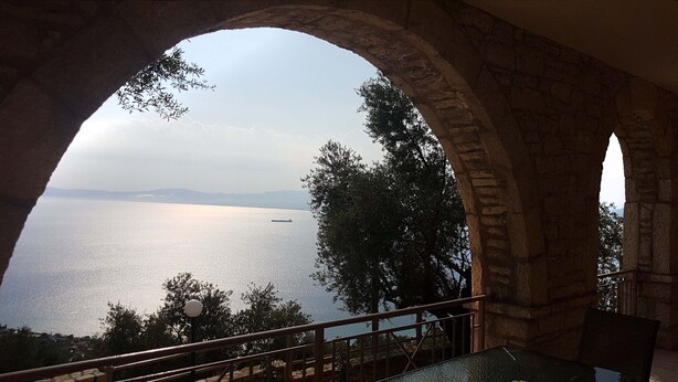 A stone archway overlooking a calm sea with distant mountains. - Olive Stonehouse Orestis (Kalamata)