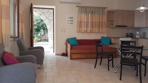A living room with a sofa, chairs, a dining table, and a kitchen area with cabinets and appliances. - Olive Stonehouse Orestis (Kalamata)