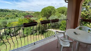 Un balcón con mesa y sillas, con vistas a un jardín exuberante y colinas lejanas.