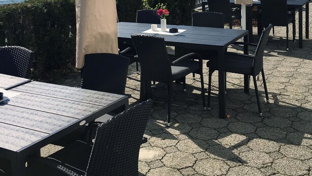 An outdoor seating area with tables and chairs, overlooking a body of water with boats and houses in the background. - Havly Bed & Breakfast (Bremanger)