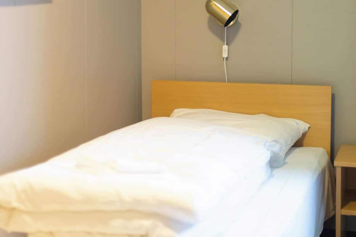 Una cama bien hecha con sábanas blancas, una mesita de noche, una lámpara y un cuadro en la pared.