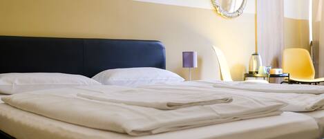 A neatly made bed with white linens, a dark headboard, and a bedside table with a lamp and a small vase.