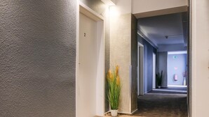 Un passadís amb una paret amb relleu, una porta amb la indicació '2' i una planta en test amb herba alta.
